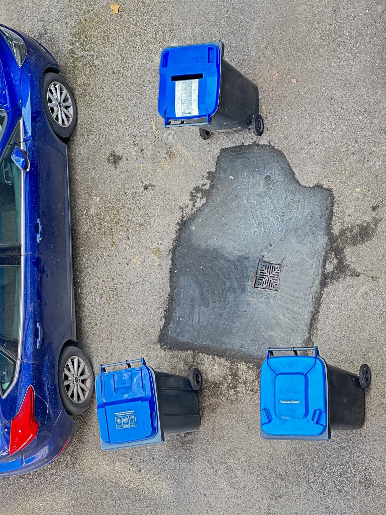 Image of tarmac with cement repair surrounded by garbage bins